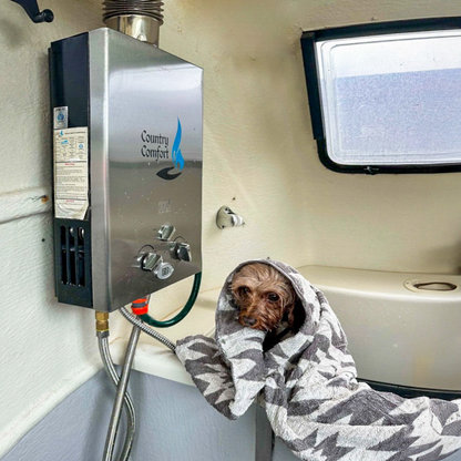 Dog wrapped in a towel in front of a Country Comfort water heater in a vehicle.